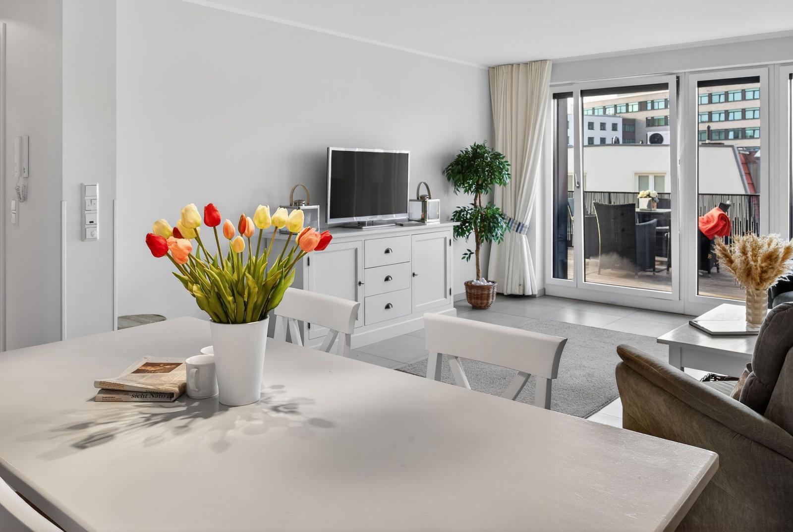 Wohnbereich mit Essbereich, Fernseher und Balkon mit Sitzgelegenheiten.