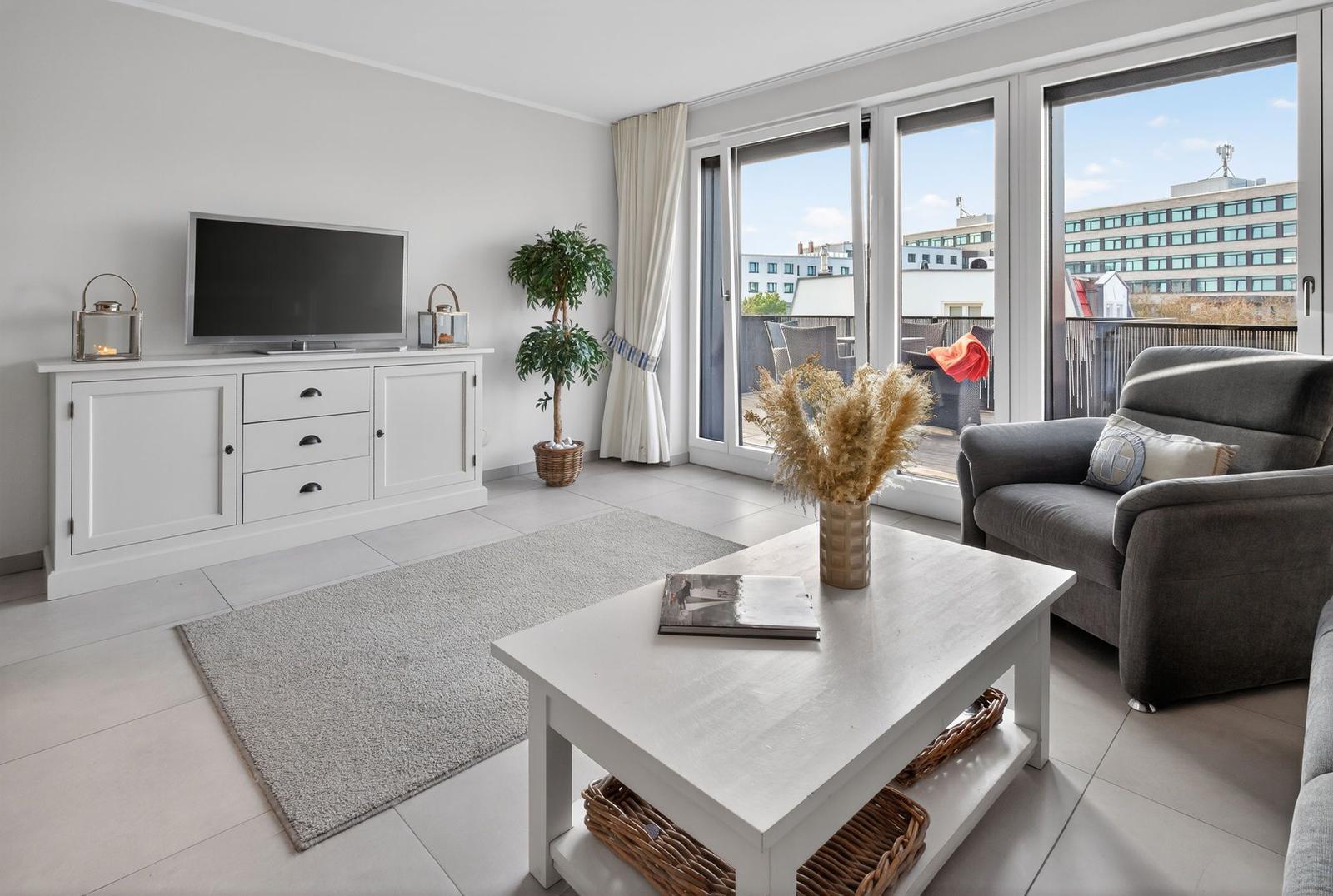 Wohnzimmer mit Fernseher, Couch und Balkon. Blick auf Stadt.