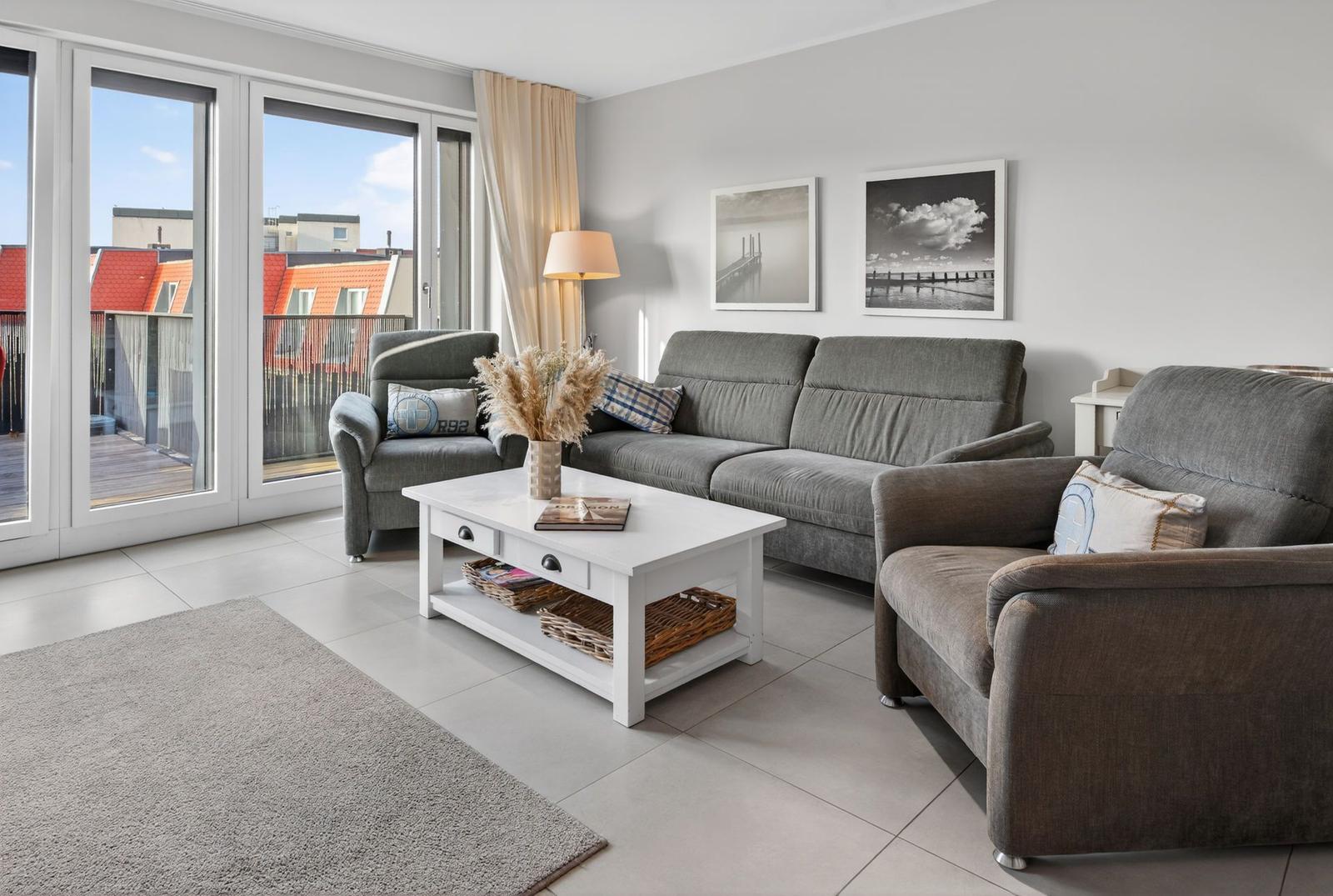Wohnzimmer mit grauen Sofas, weißem Couchtisch und Blick auf Balkon.