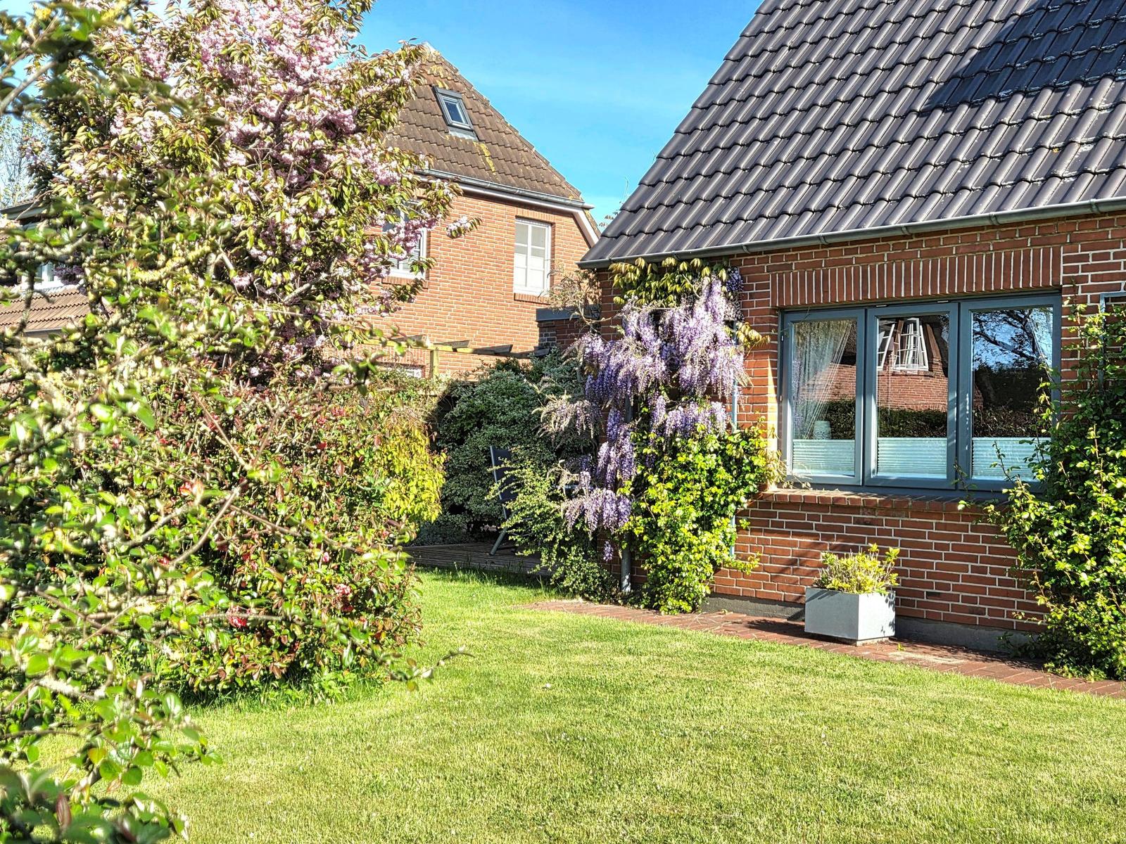 Rotes Backsteingebäude mit Gartenterrasse und blühenden Sträuchern im Vordergrund.