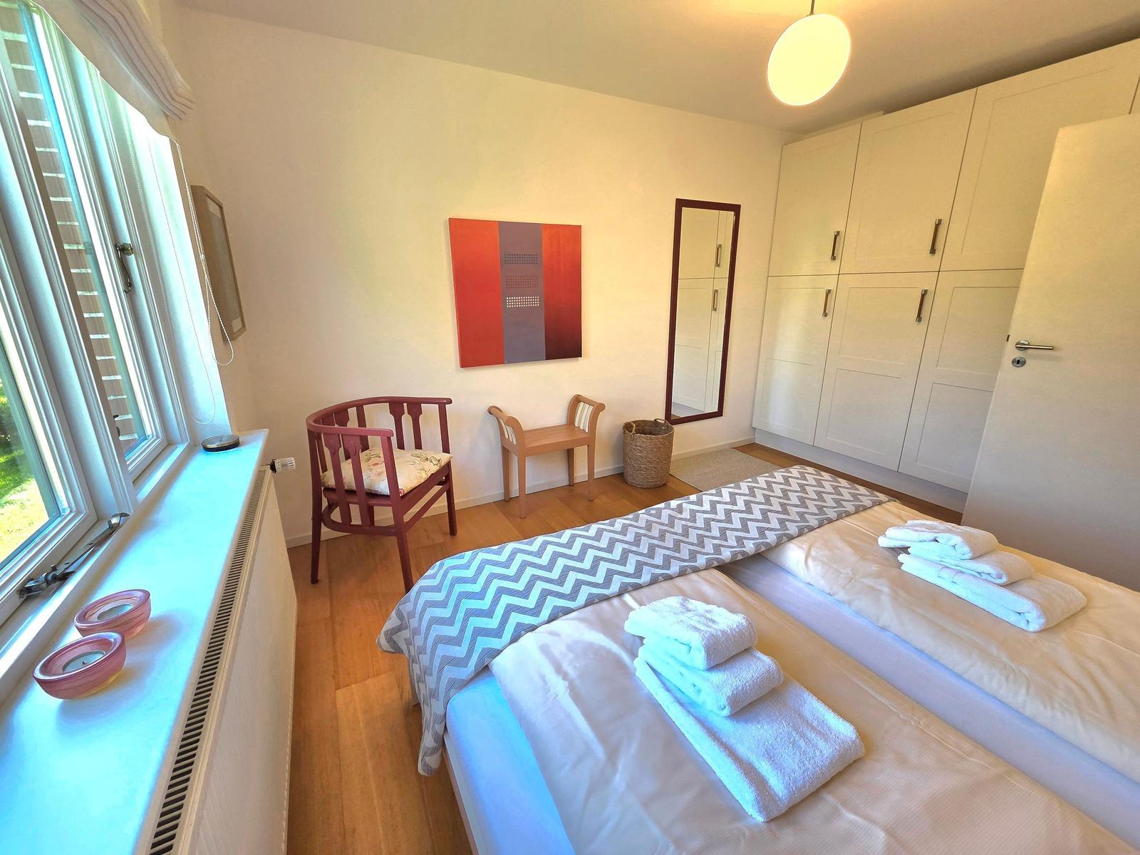Zimmer mit zwei Betten, Schrank, Stuhl und Fenster. Handtücher ordentlich aufgebettet.