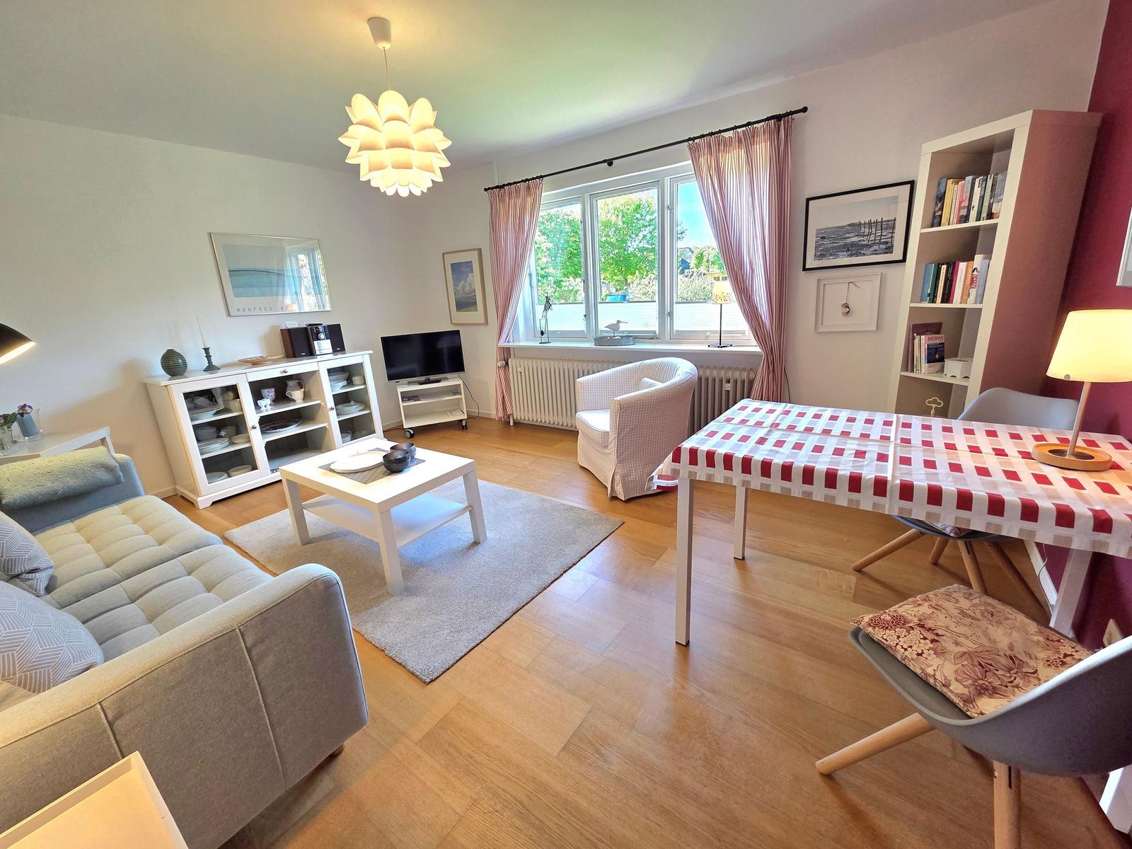 Wohn- und Essbereich mit Sofa, Esstisch und Fenster. Holzboden und Bücherregal.