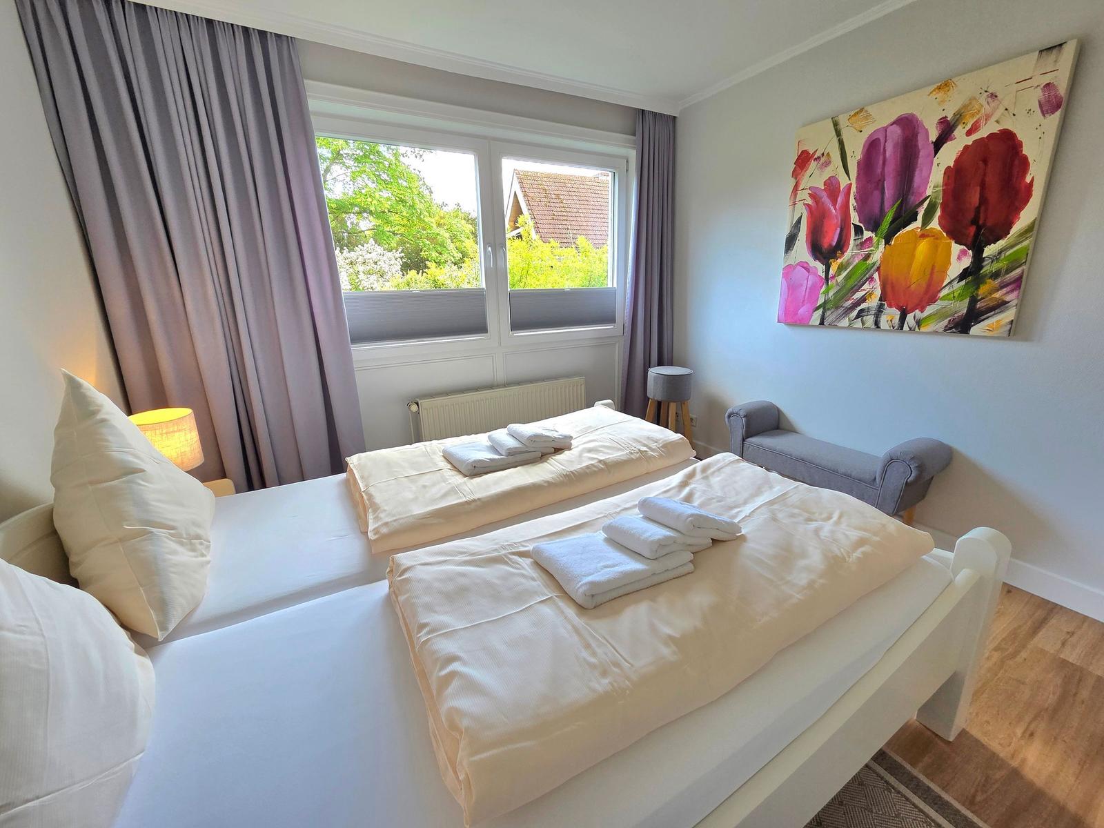 Zimmer mit Doppelbett, Fenster, Wandbild und Sitzbank.