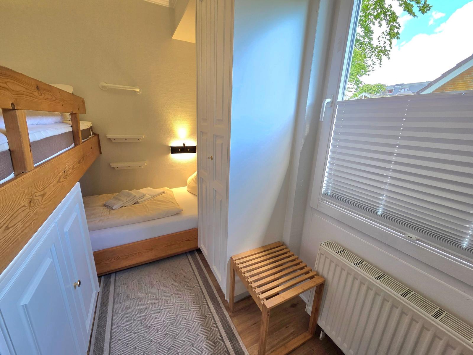 Zimmer mit Doppelbett, Etagenbett und Fenster mit Jalousie.