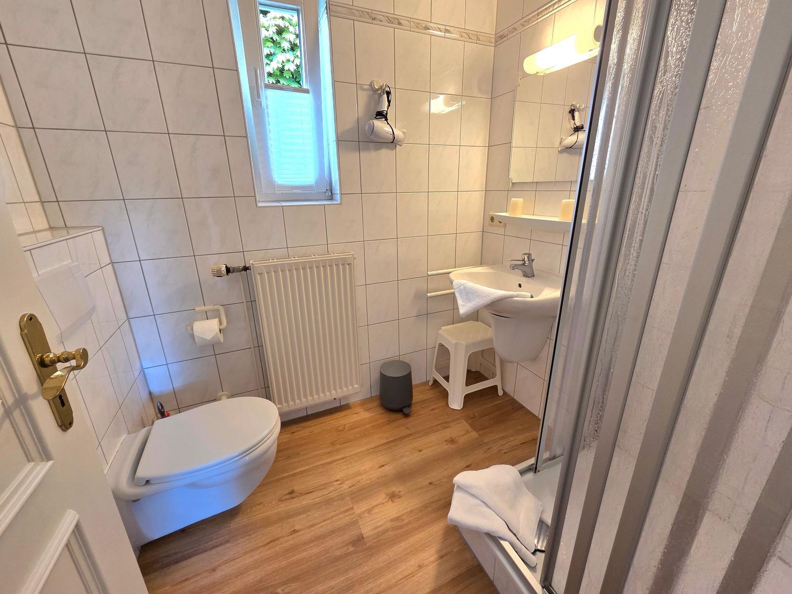 Badezimmer mit Toilette, Waschbecken und Dusche. Holzboden und Fenster mit Blick.
