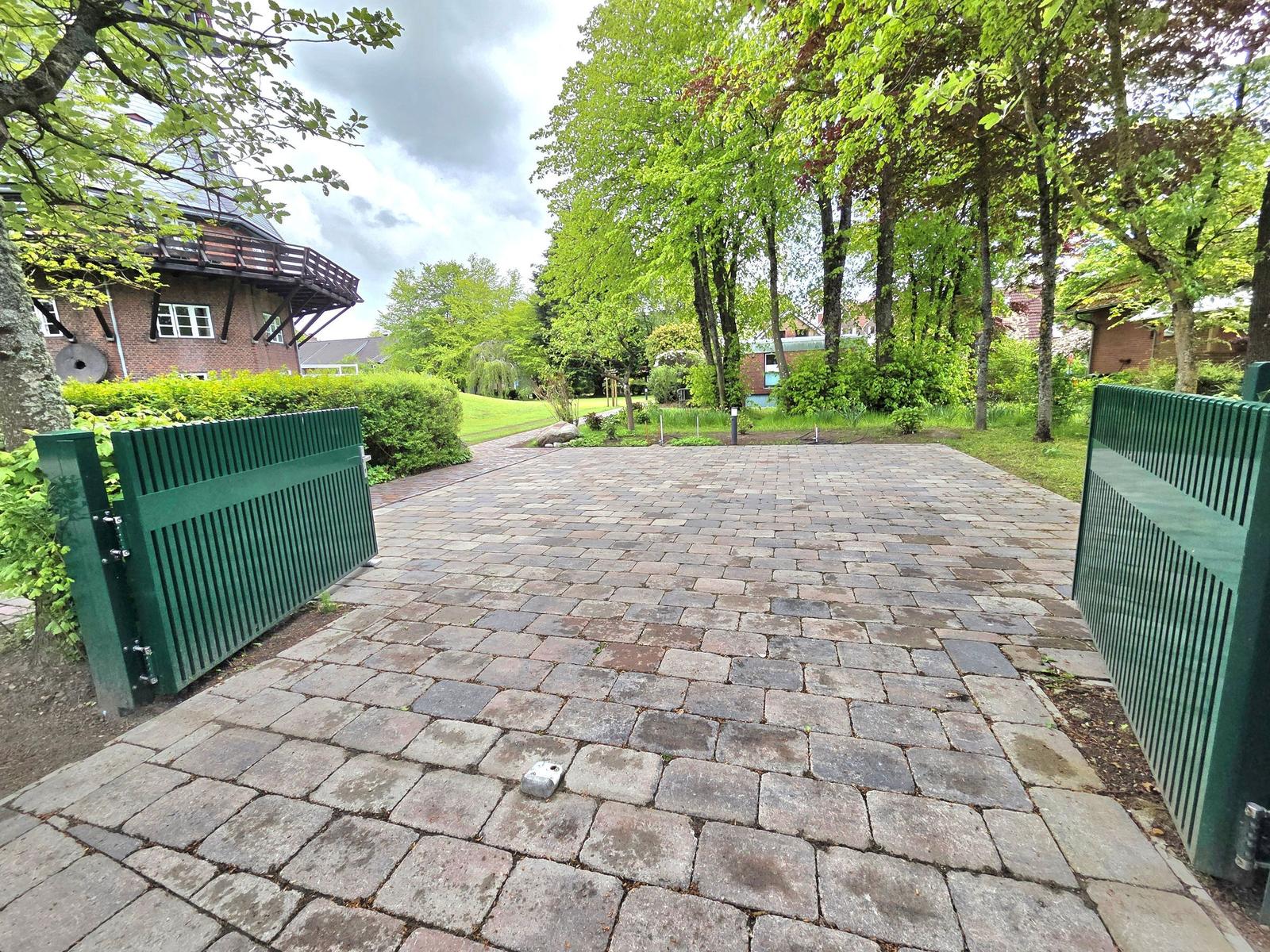 Pflasterter Weg mit grünen Toren führt zu einem Haus im Grünen.