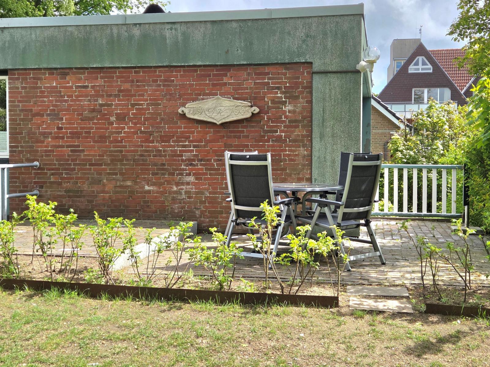 Terrasse mit Tisch und zwei Stühlen vor Backsteinwand mit Holzschild.