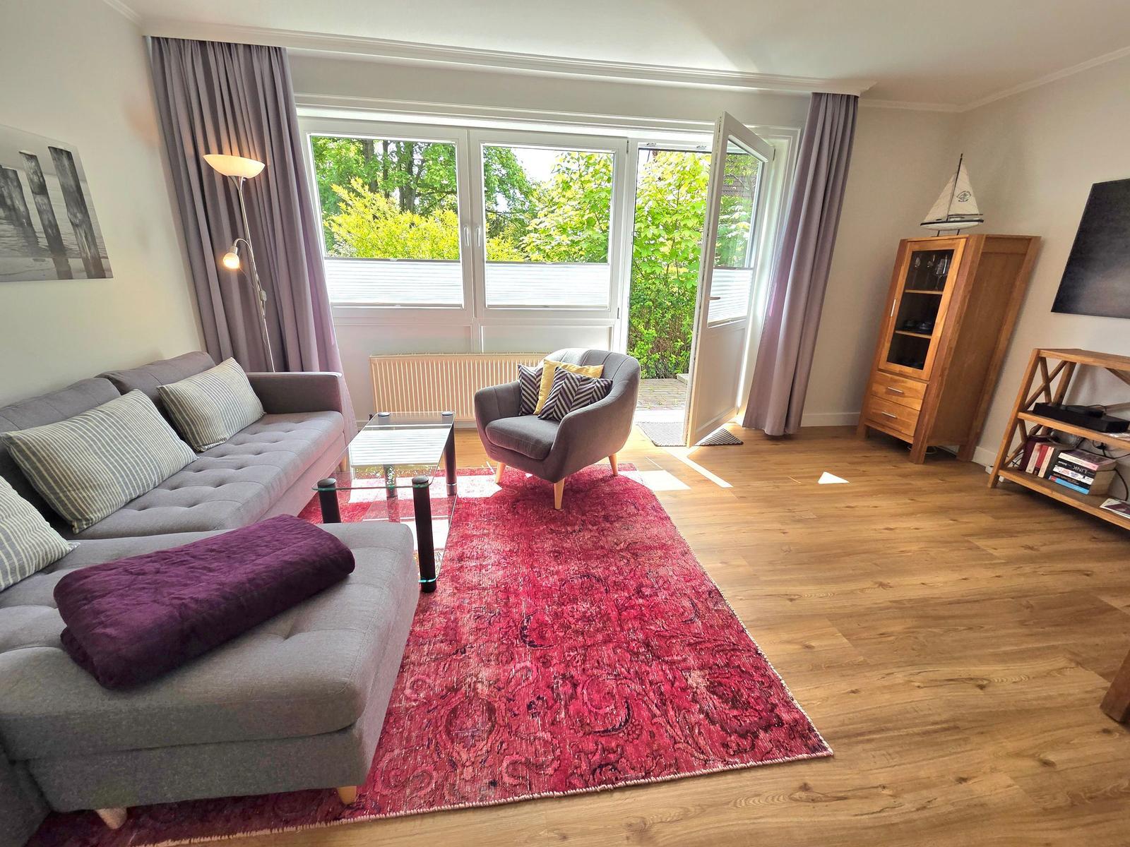 Wohnzimmer mit Sofa, Sessel, Teppich und Blick auf Garten