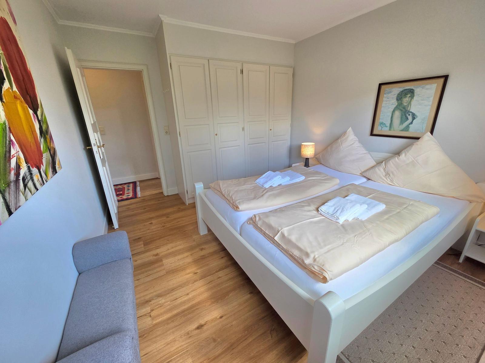Schlafzimmer mit Doppelbett, Kleiderschrank und Sitzgelegenheit.