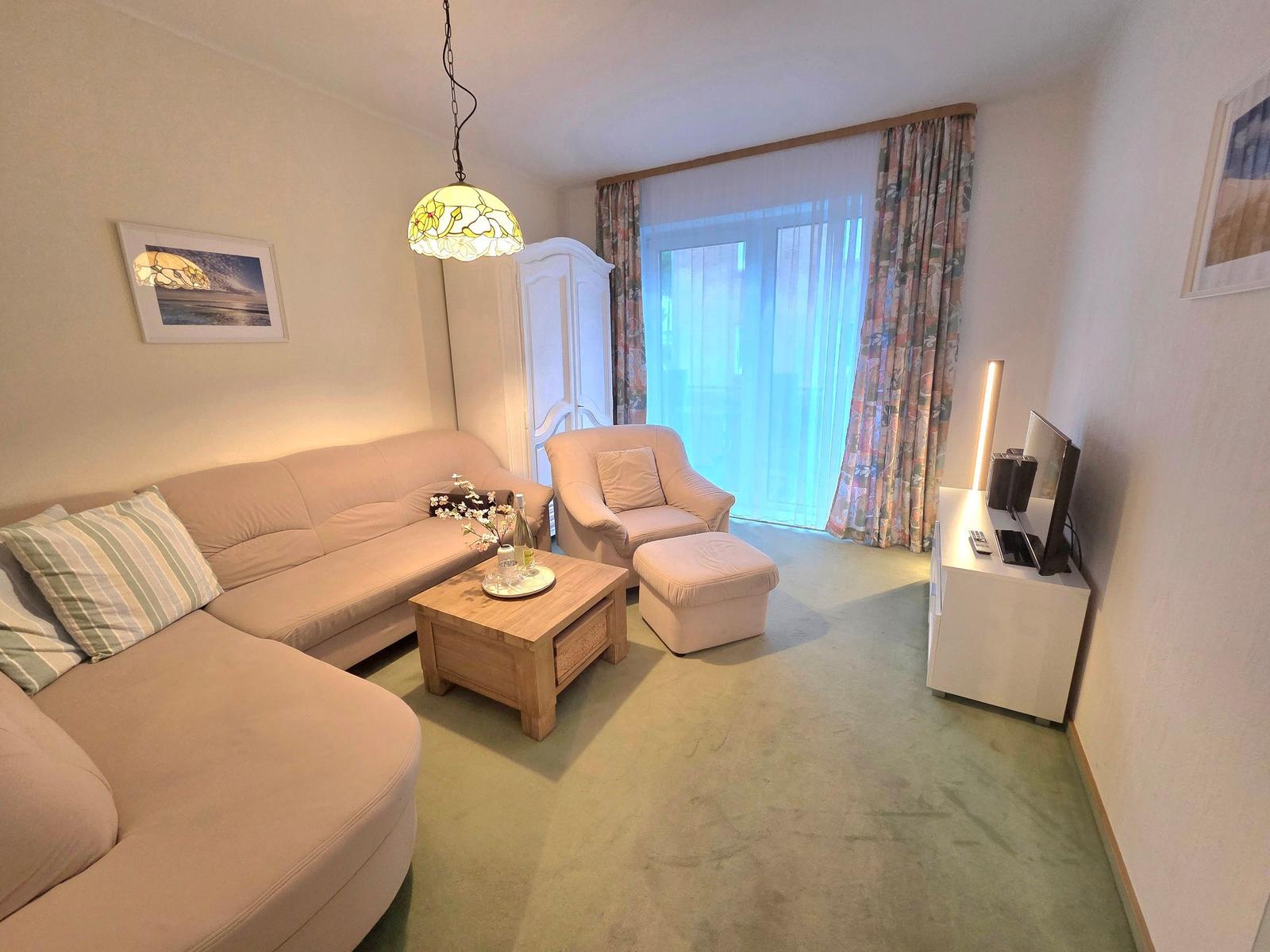 Wohnzimmer mit Sofa, Sessel, Couchtisch und TV. Fenster mit Vorhängen.