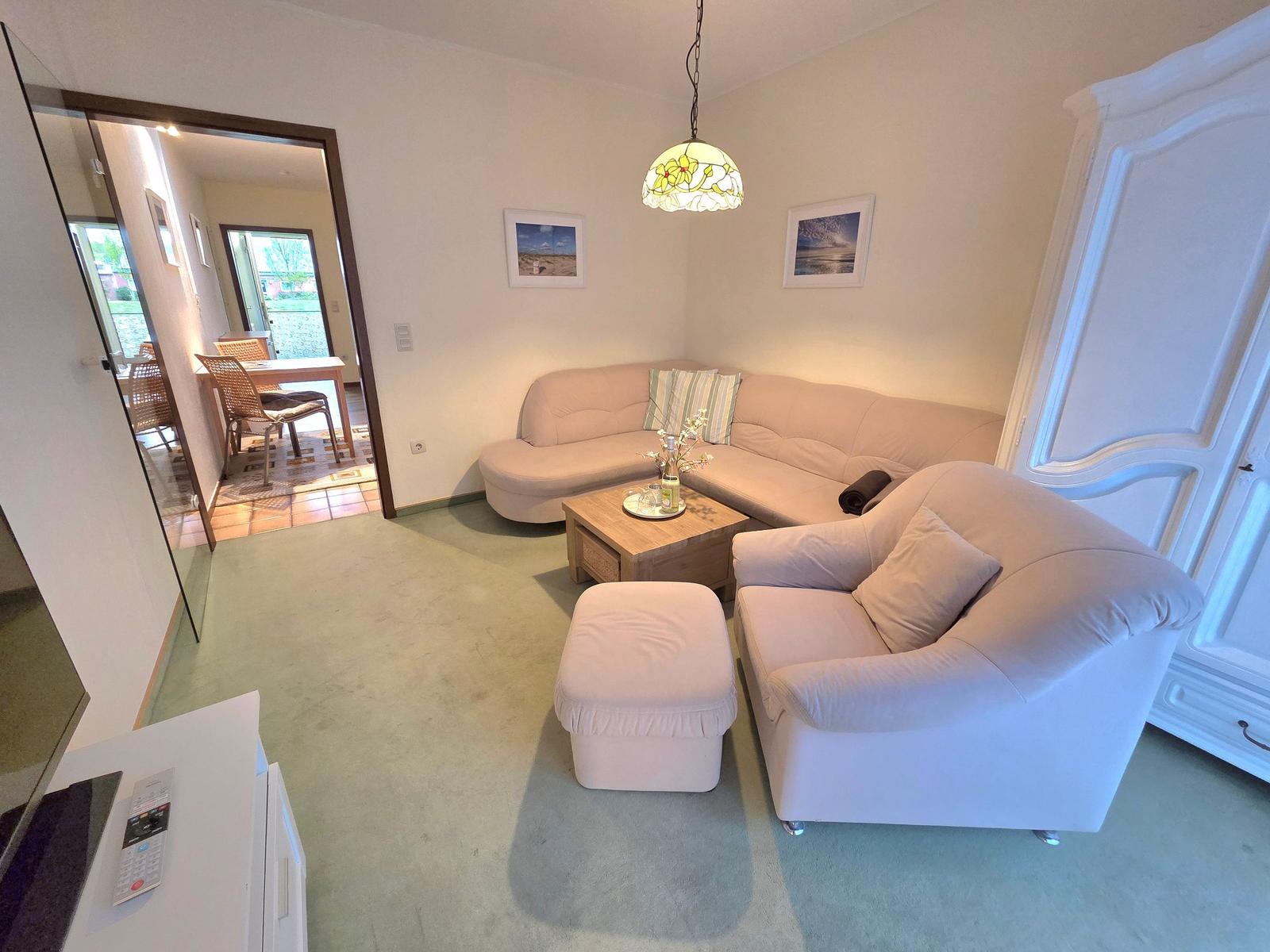 Wohnzimmer mit Sofa, Sessel und Holztisch. Durchgang zur Küche und Terrasse.