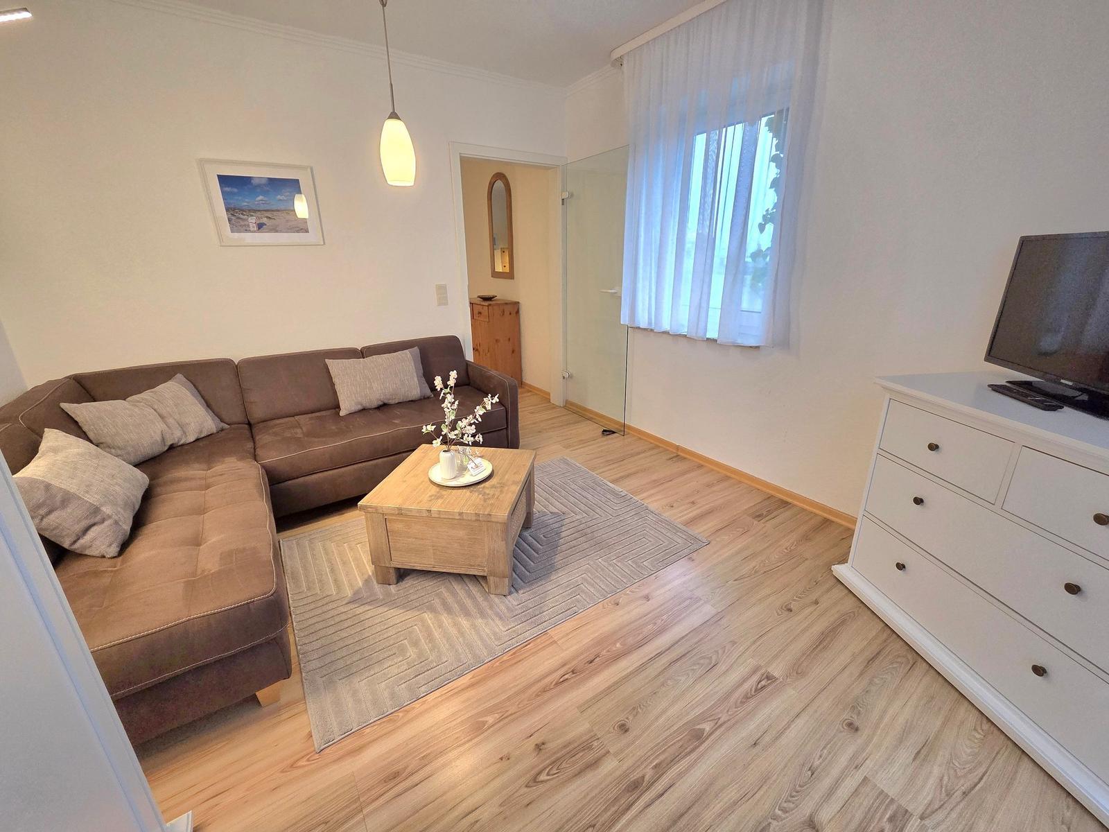 Wohnzimmer mit braunem Sofa, Holztisch und Fernseher auf weißen Schrank.