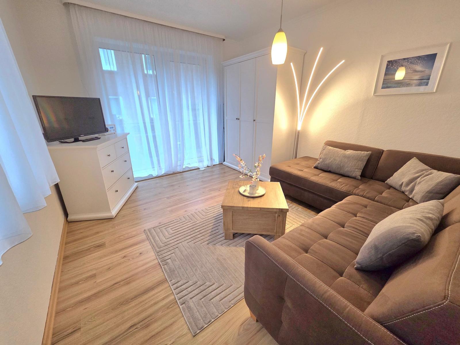 Wohnzimmer mit braunem Sofa, Holztisch und Fernseher auf weißen Schrank.