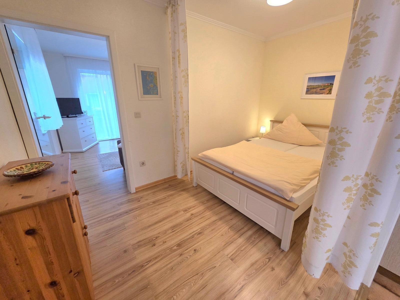 Schlafzimmer mit Bett, Holzboden und Blick in Wohnbereich.