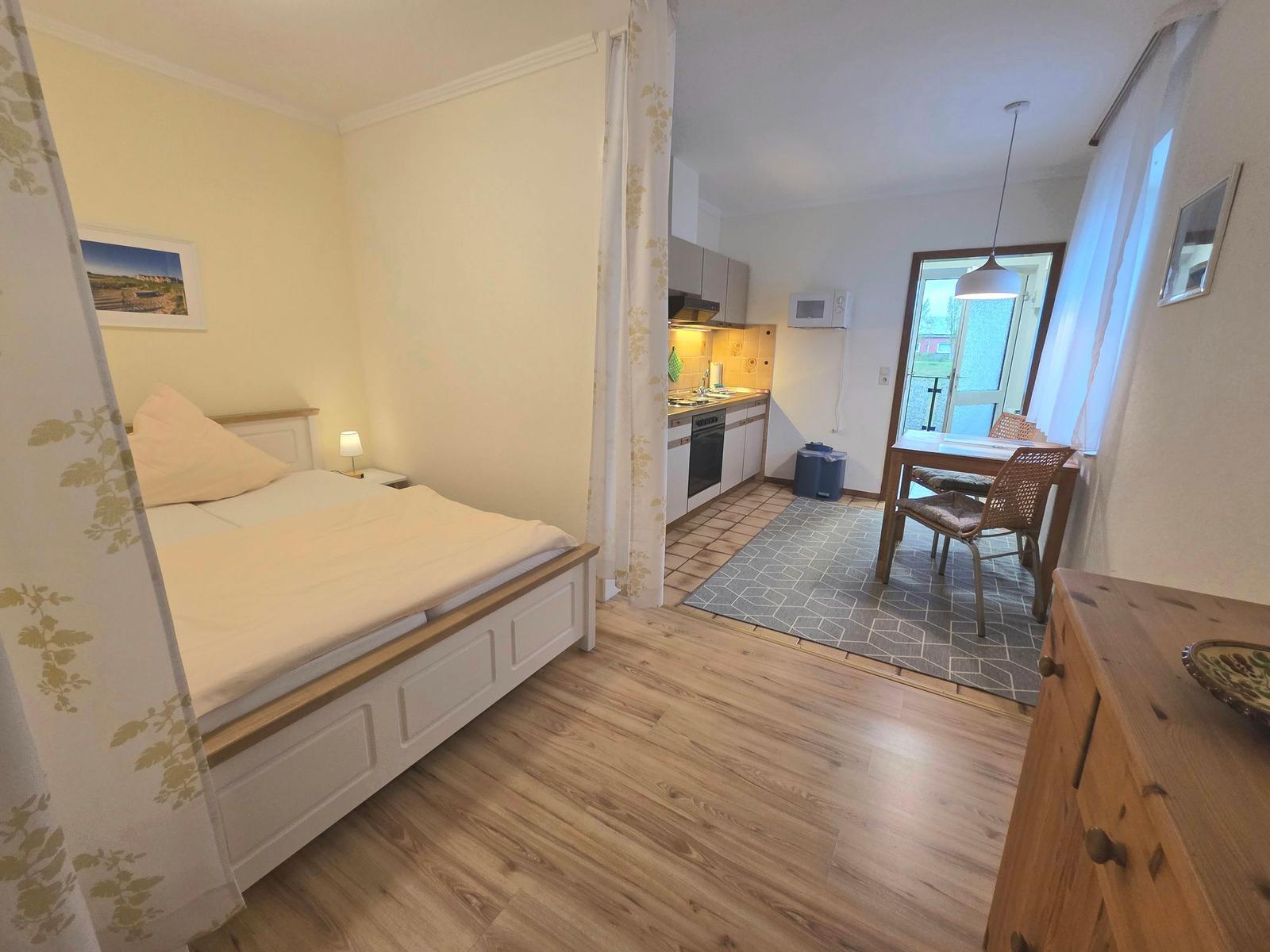 Schlafzimmer mit Bett und Wohnbereich mit Küchenzeile und Esstisch.