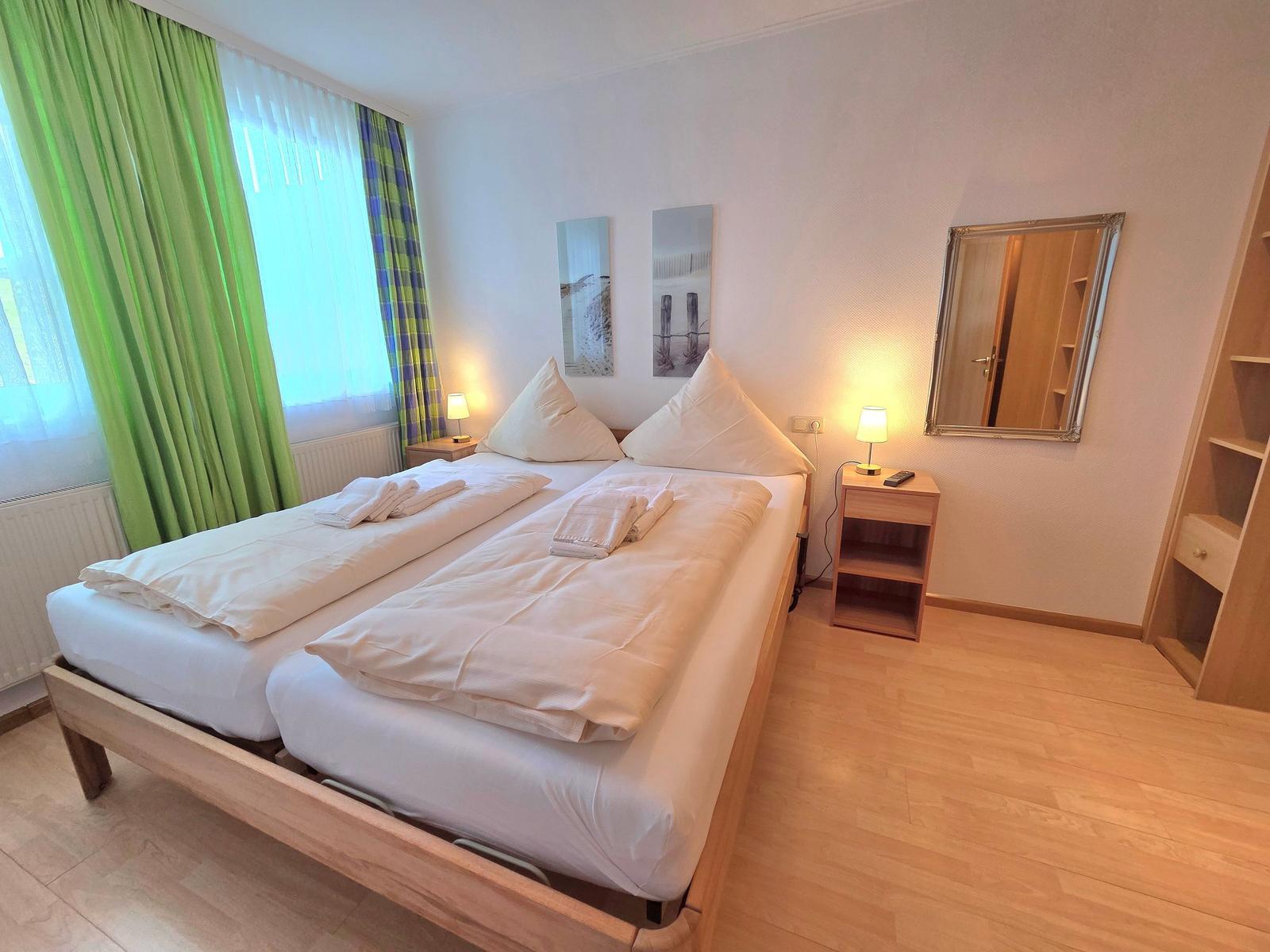 Doppelbett mit weißen Bettwäsche, Nachttische mit Lampen und Spiegel an der Wand.