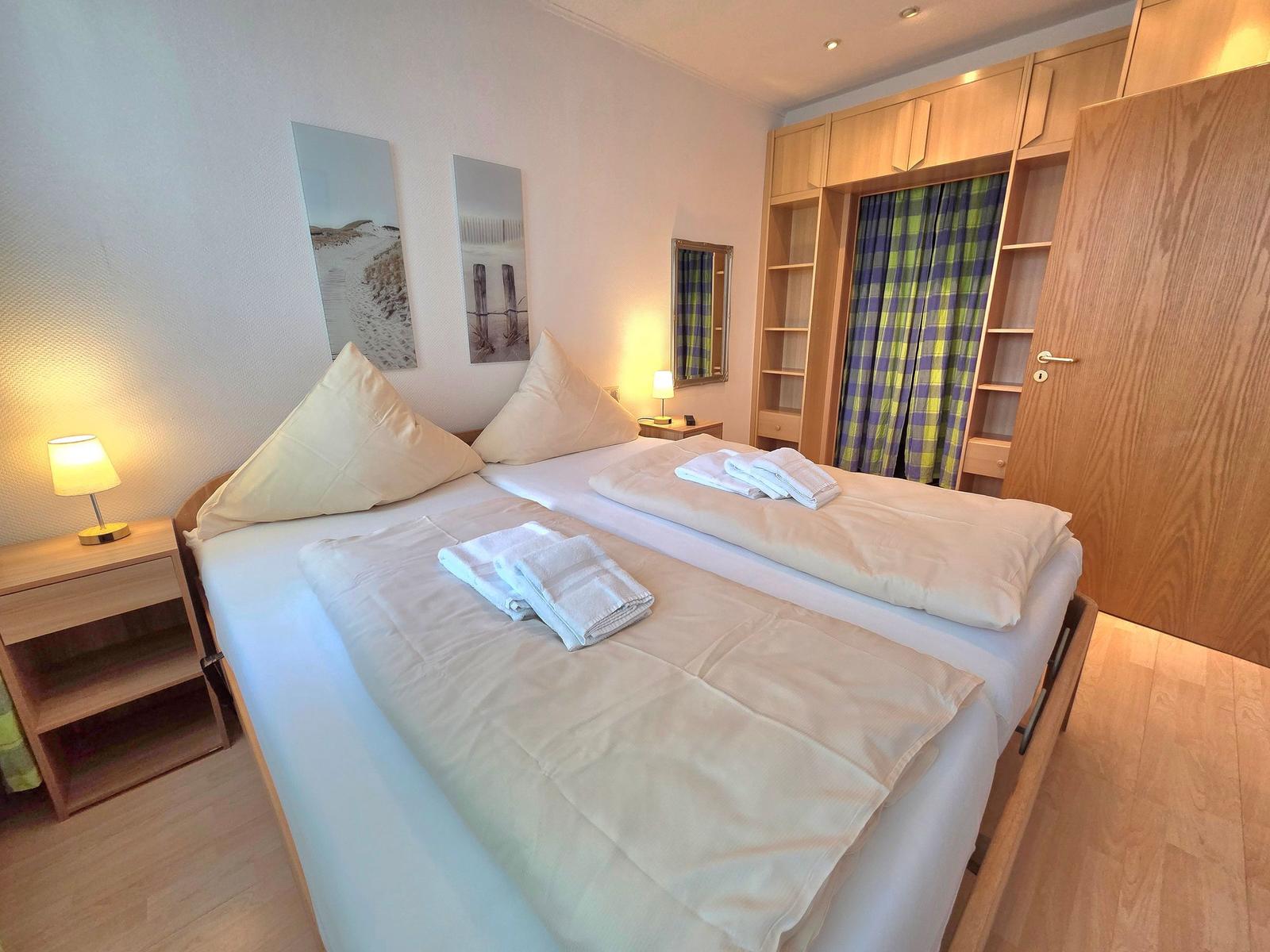 Schlafzimmer mit Doppelbett, Holzmöbel und Plaidvorhängen.