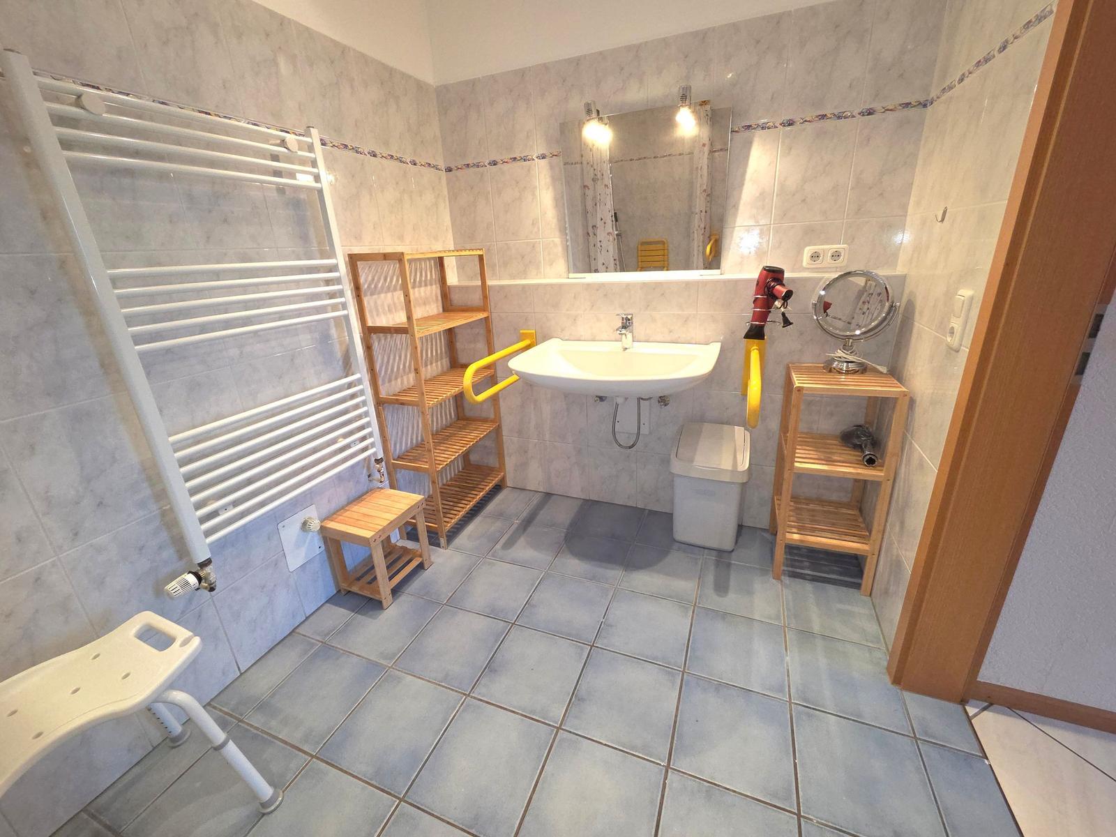 Badezimmer mit Duschbereich, Waschbecken, Handtuchhalter und Aufbewahrungsmöbel.