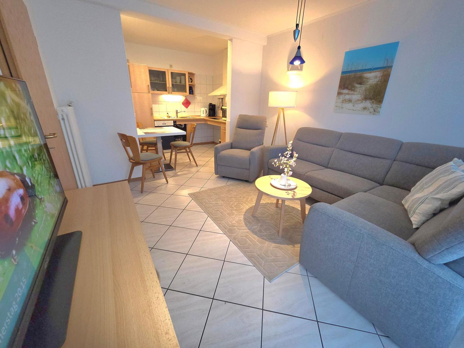 Wohnzimmer mit Sofa, Sessel und Küchenbereich im Hintergrund.