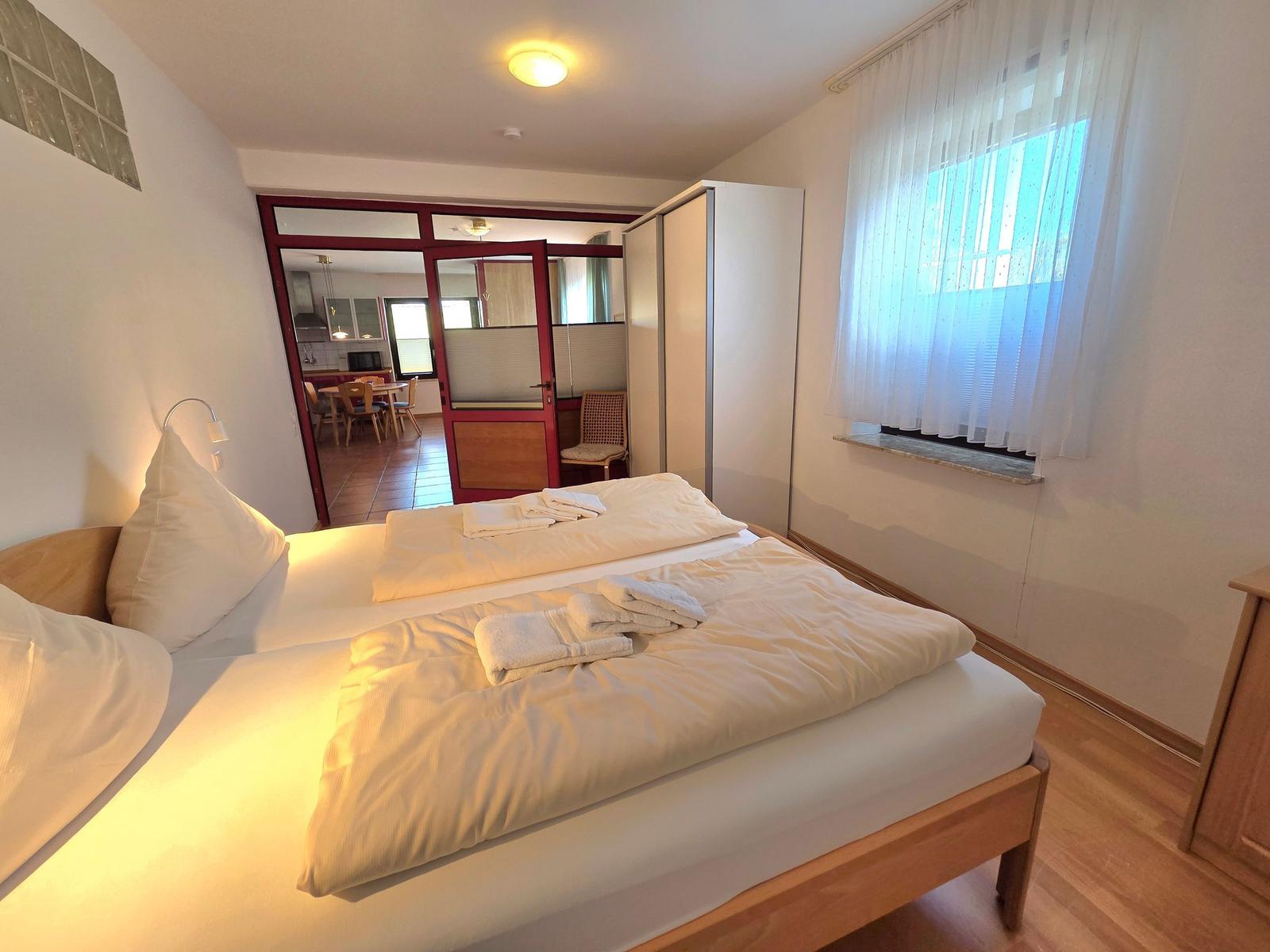 Bedroom with double bed, window, and view into the kitchen.