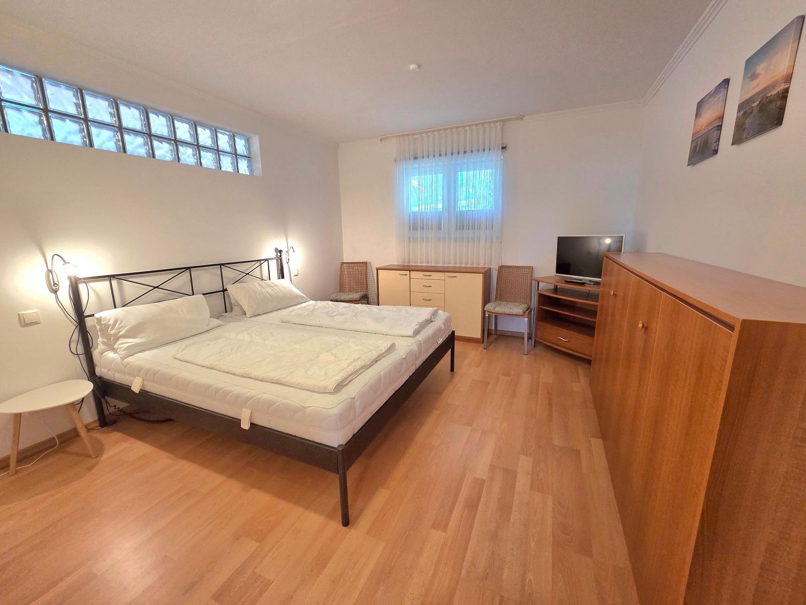Bedroom with double bed, wooden floor, window, and wardrobe.