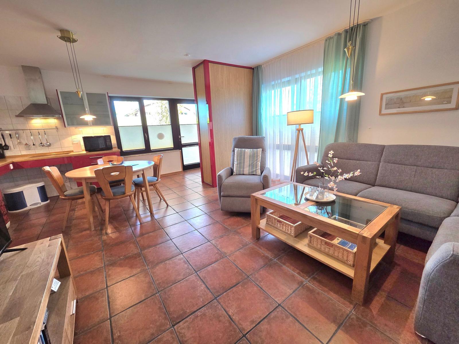 Living and dining area with sofa, armchair, dining table, and kitchen.