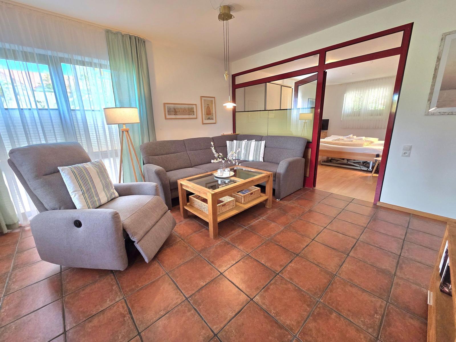 Living room with sofa, armchair, and table. Passage to bedroom with bed.