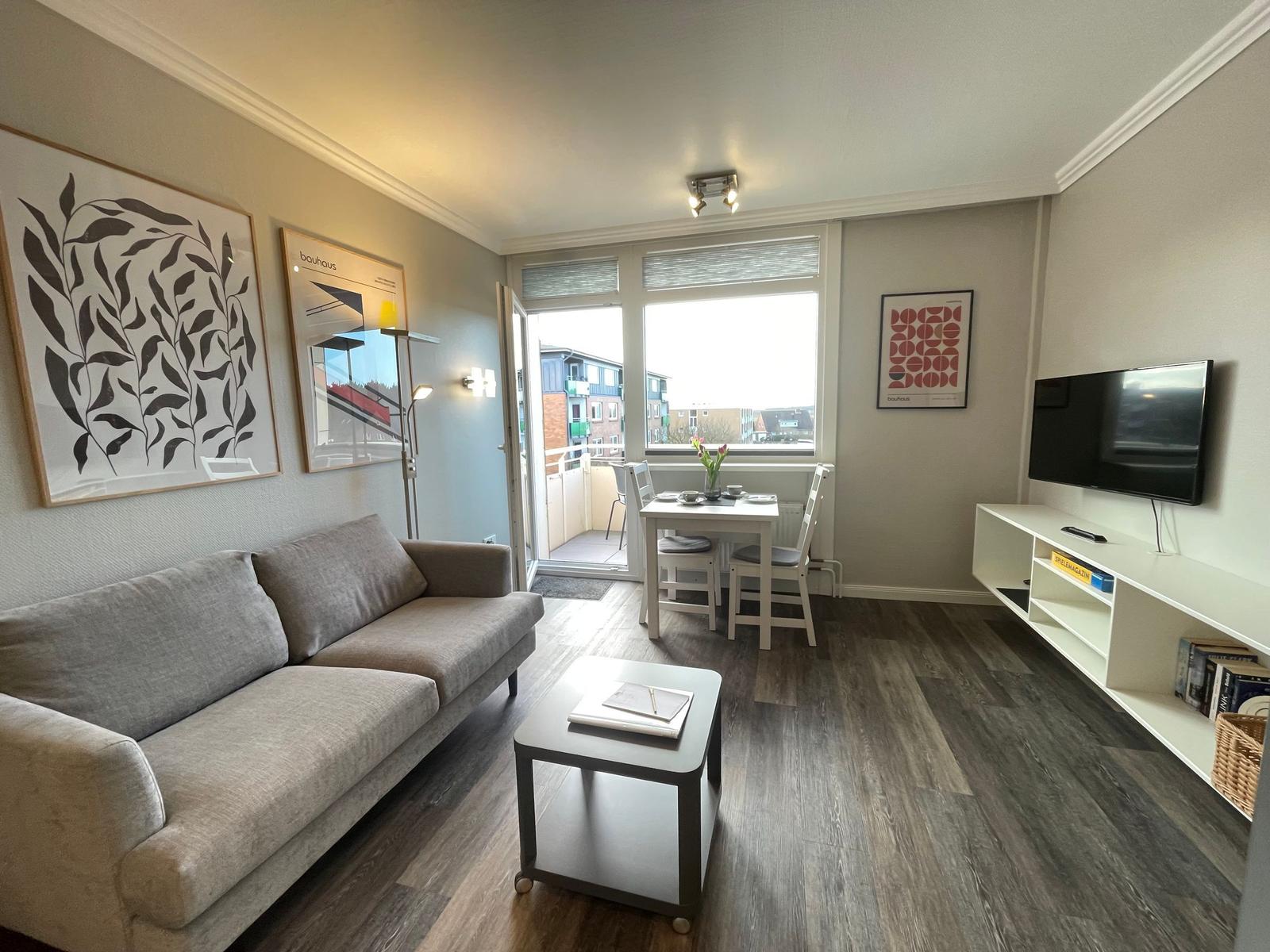 Wohnzimmer mit Sofa, Esstisch und Fernseher an der Wand.