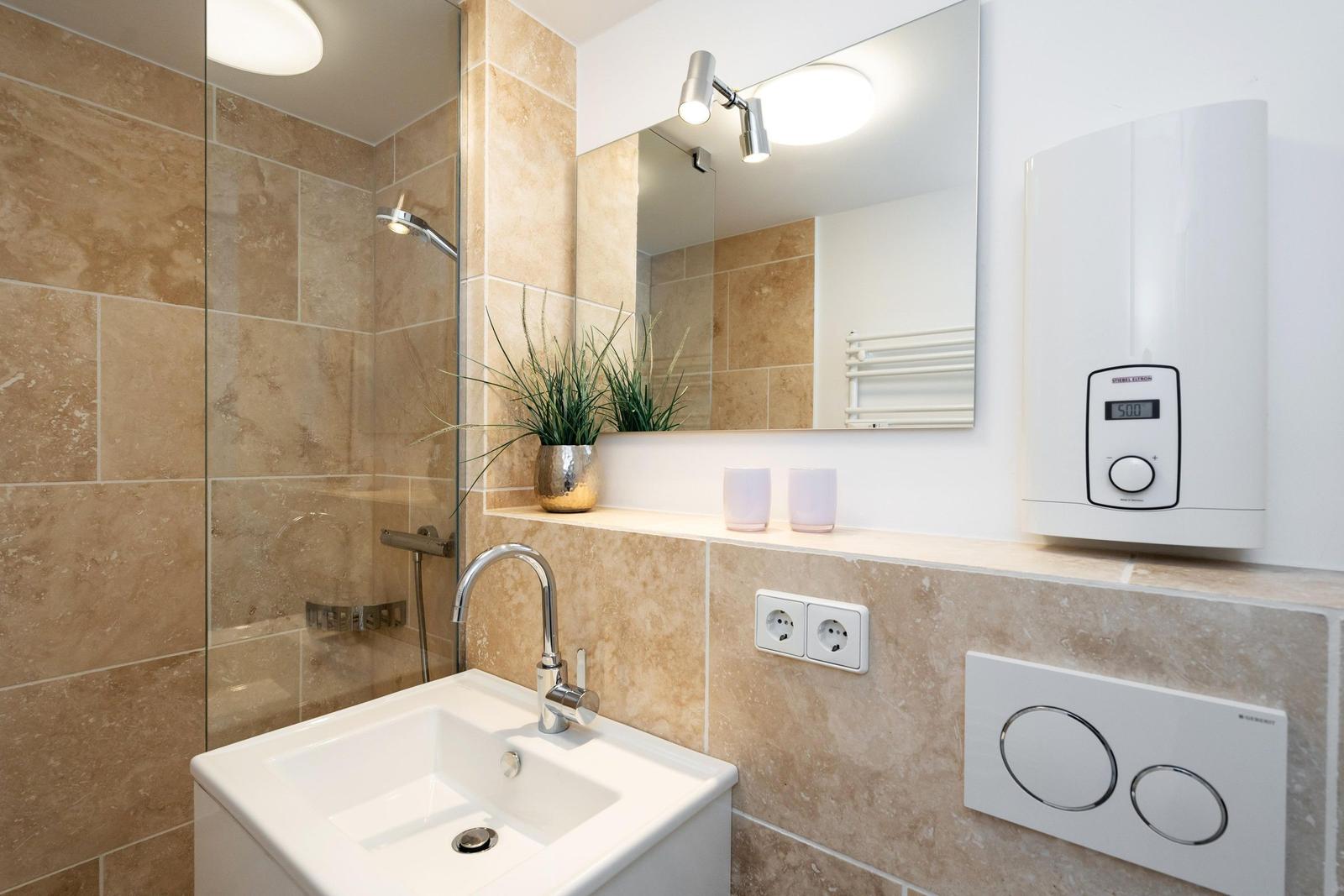 Badezimmer mit Dusche, Waschbecken und Spiegel.