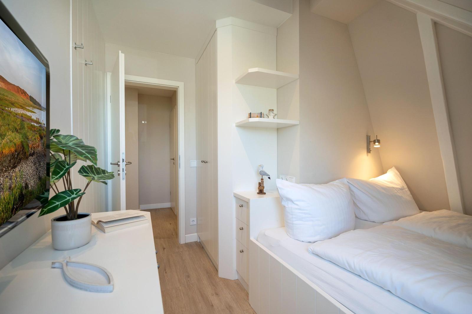 Schlafzimmer mit Bett, Schrank und Fernseher. Holzfußboden und weiße Möbel.