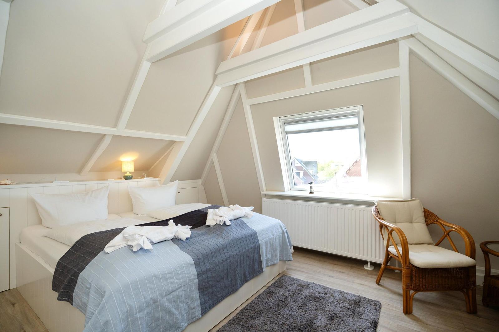 Schlafzimmer mit Dachschrägen, Bett, Stuhl und Fenster.
