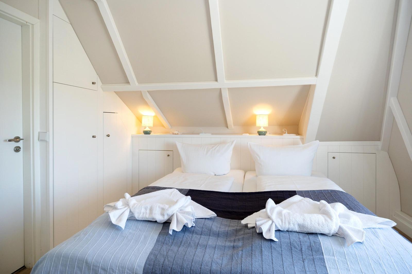 Schlafzimmer mit Dachschrägen, Bett mit weißen Kissen und zwei Handtüchern.