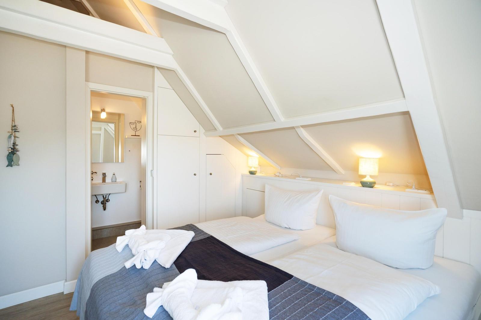 Schlafzimmer mit Dachschrägen, Bett, Nachttisch und angrenzender Badewanne.