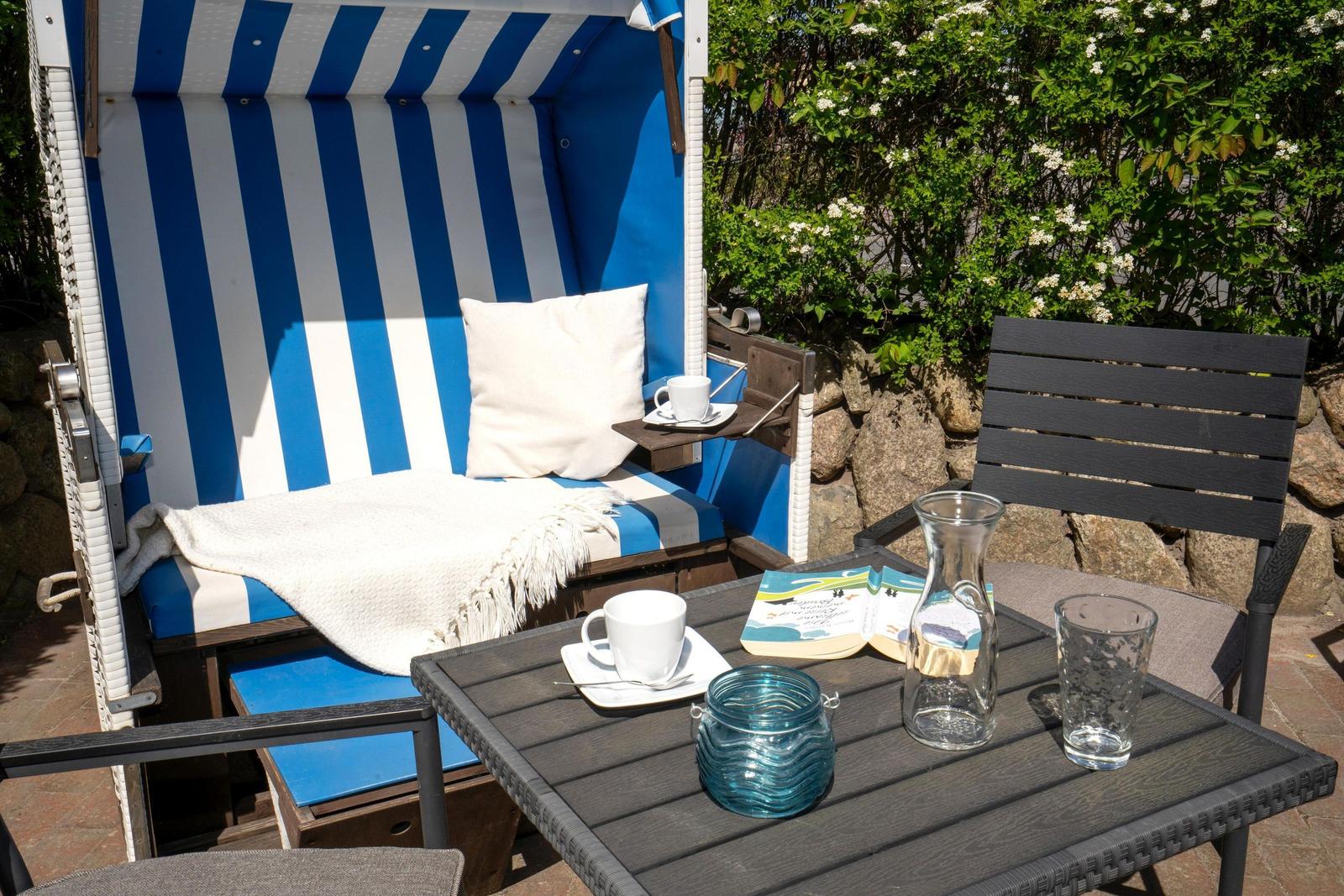 Blau-weiße Strandliege mit Kissen und Tisch mit Tassen und Buch.