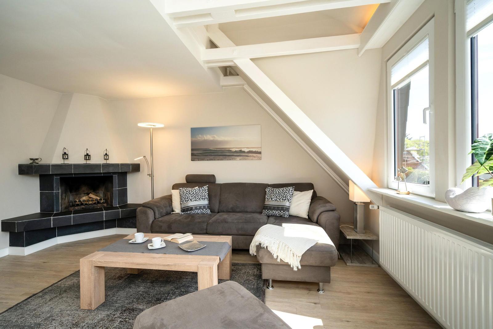 Wohnzimmer mit Sofa, Kamin und großem Fenster. Holzboden und Deckenbalken.