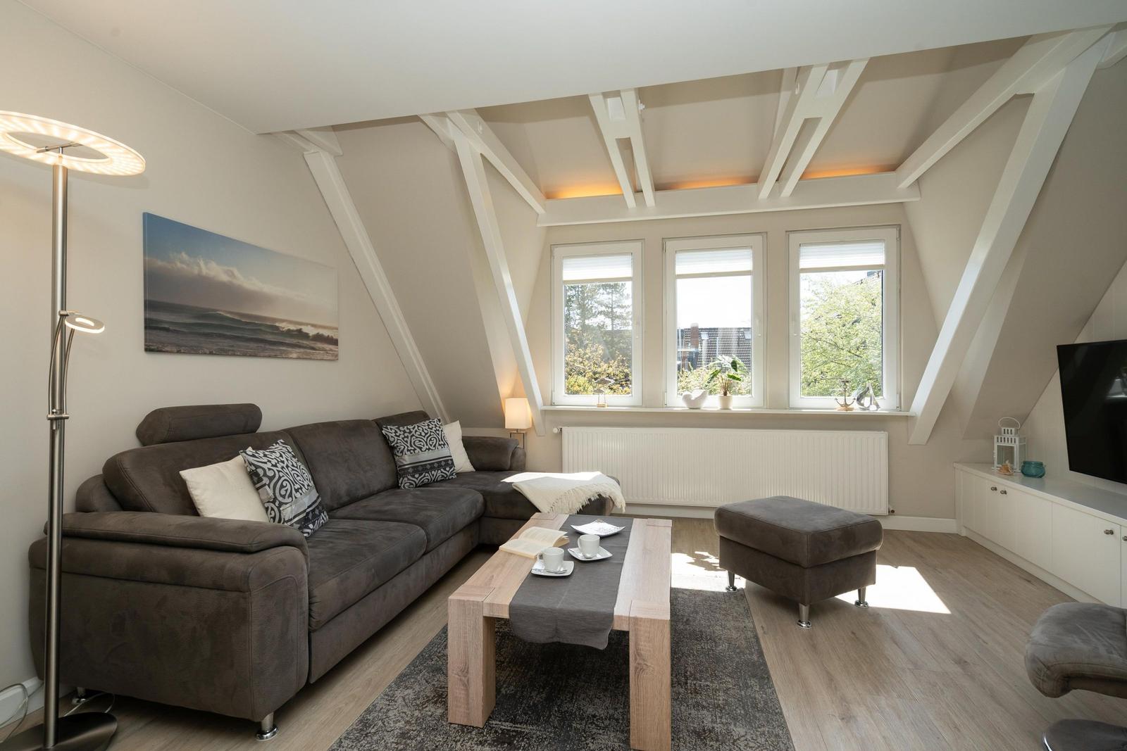 Wohnzimmer mit Sofa, Couchtisch und Fenstern. Deckenbalken und Holzboden.