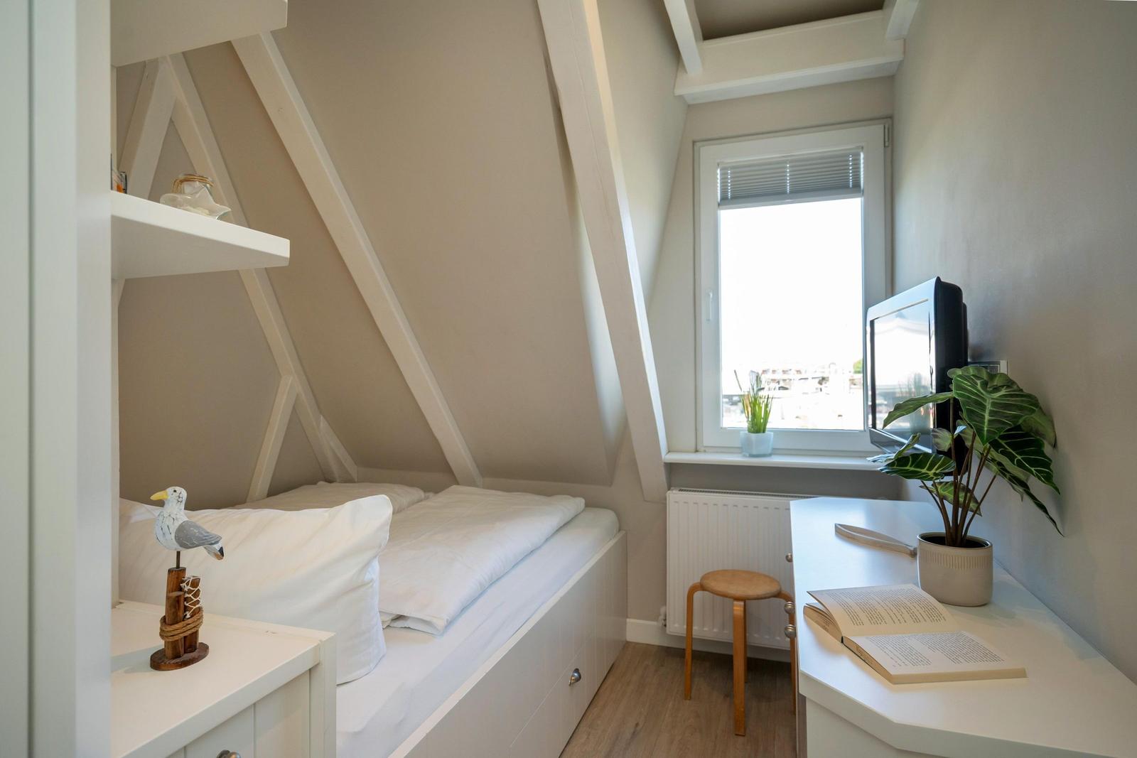 Schlafzimmer mit Dachschrägen, Bett, Schreibtisch und Fenster.