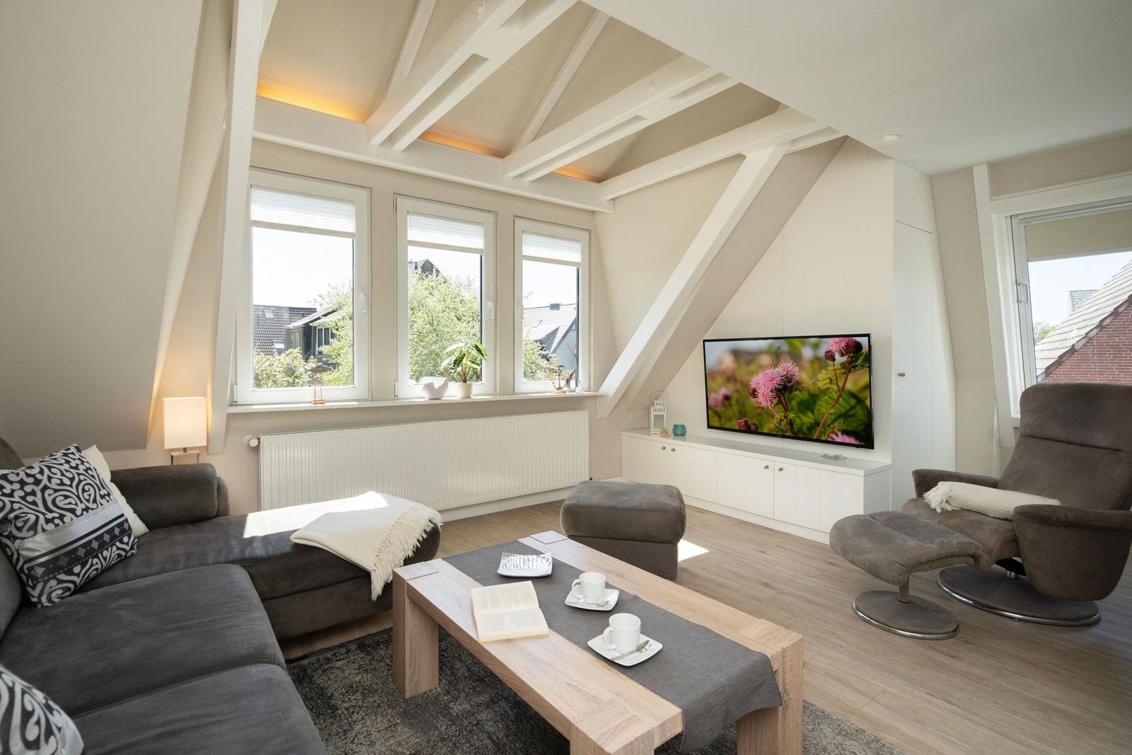 Wohnzimmer mit Sofa, Fernseher und Sessel unter Holzdecke.