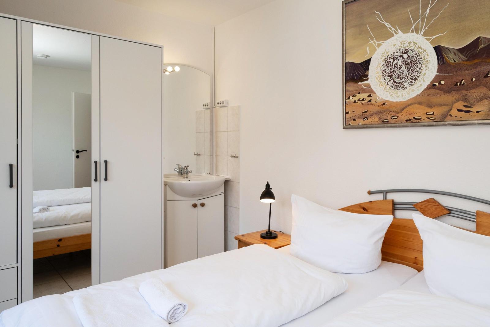 Schlafzimmer mit Bett, Nachttisch, Spiegel und Wandbild.