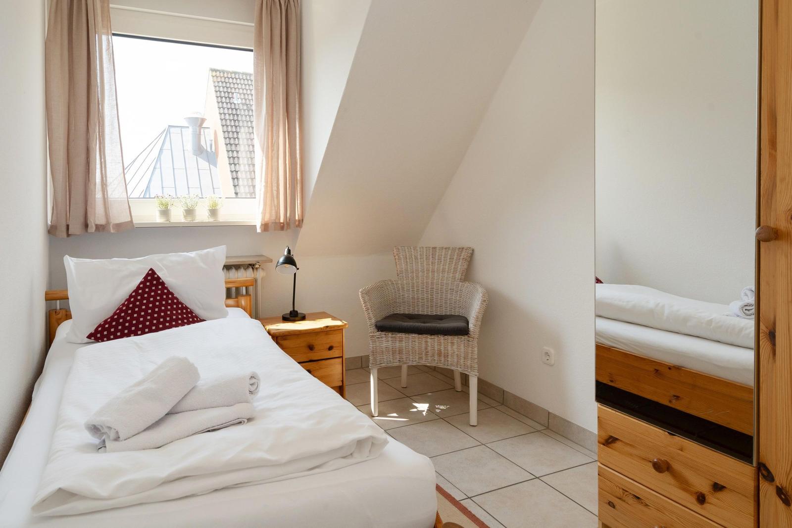 Schlafzimmer mit Dachschrägen, Bett, Stuhl und Fenster mit Blick.