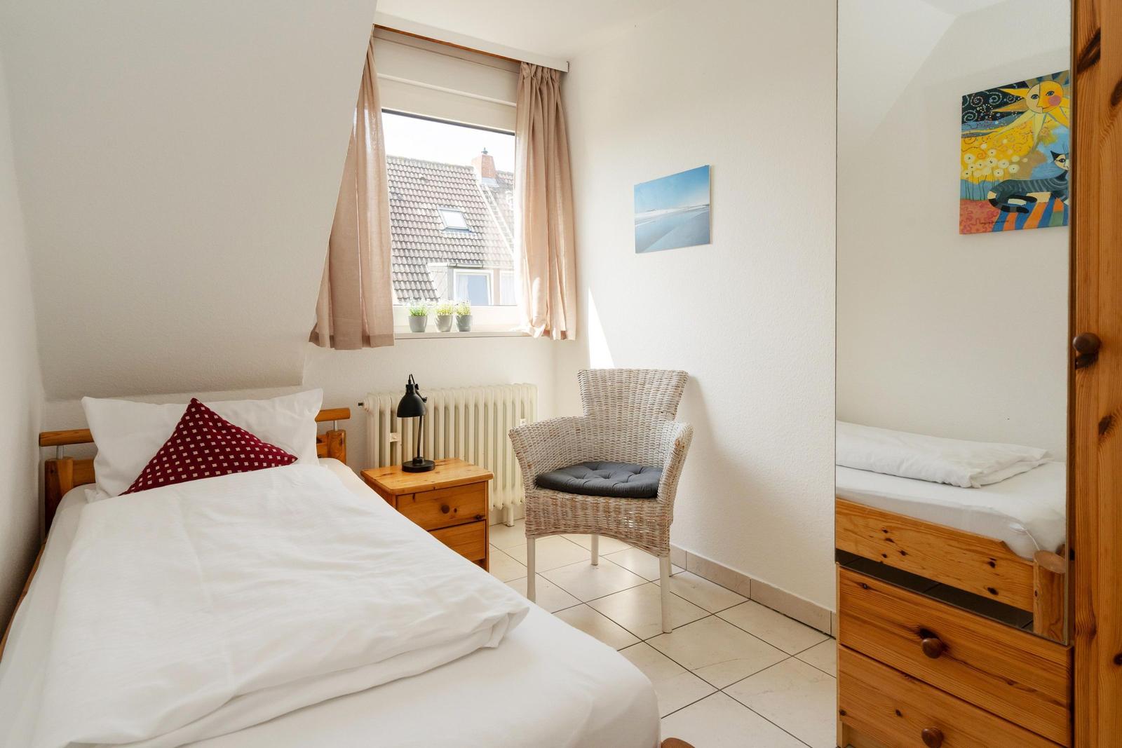 Ein Schlafzimmer mit Bett, Stuhl, Nachttisch und Fenster mit Blick auf Dächer.
