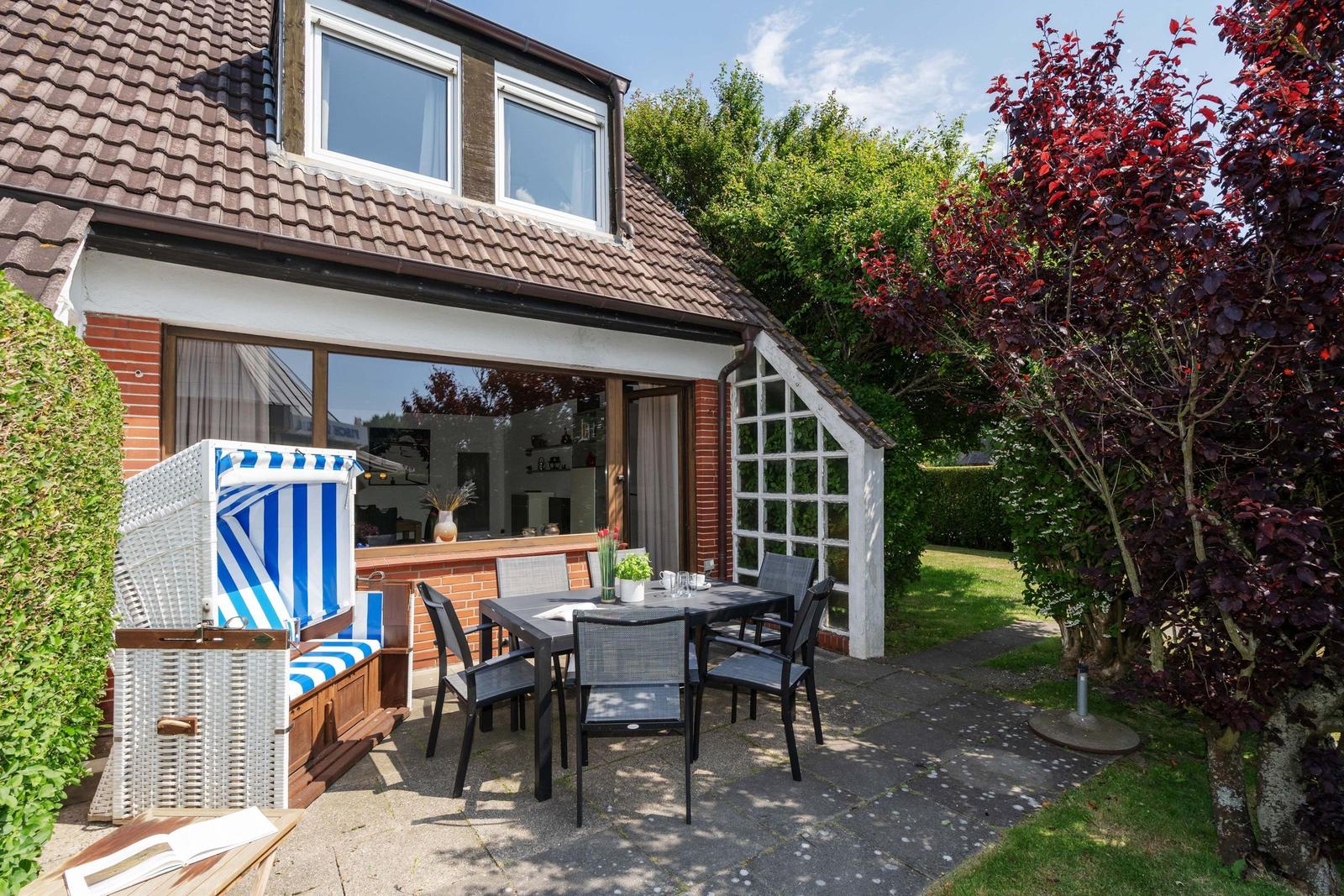 Terrasse mit Tisch, Stühlen und Strandkorb. Hinterhof mit Grünflächen und Bäumen.
