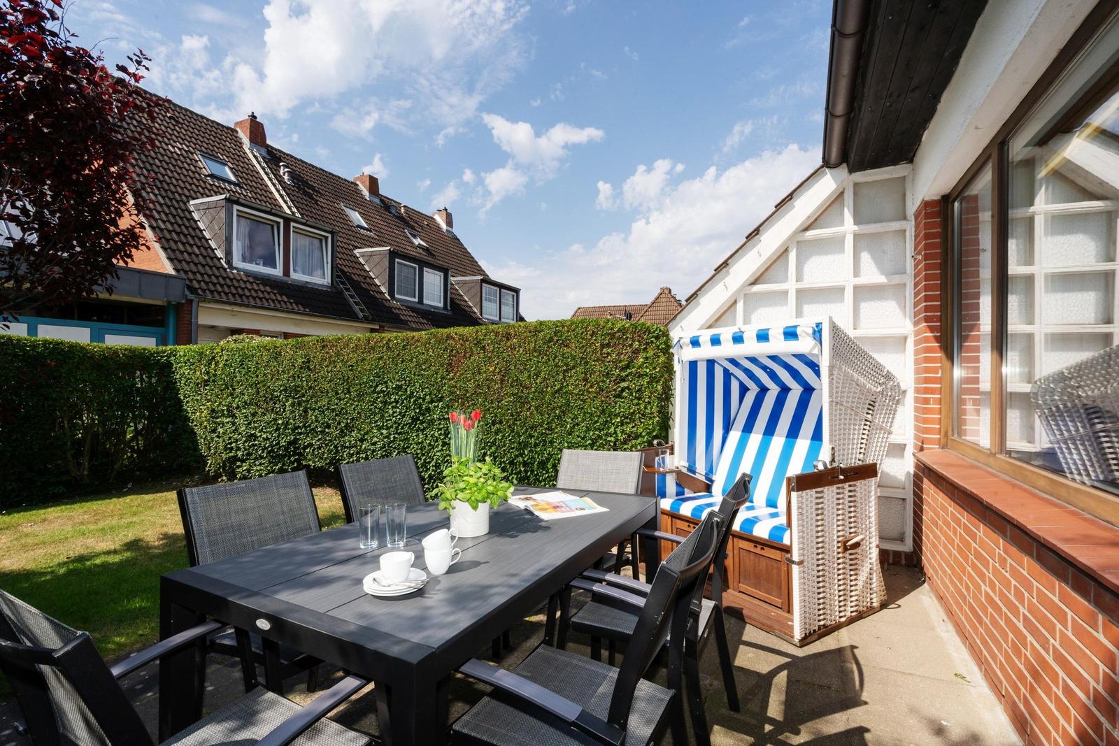 Terrasse mit Tisch, Stühlen und Strandkorb. Hinterhof mit Hecke und Garten.