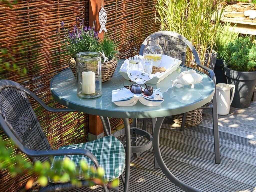 Round table with chairs on terrace, flowers and drinks on top.