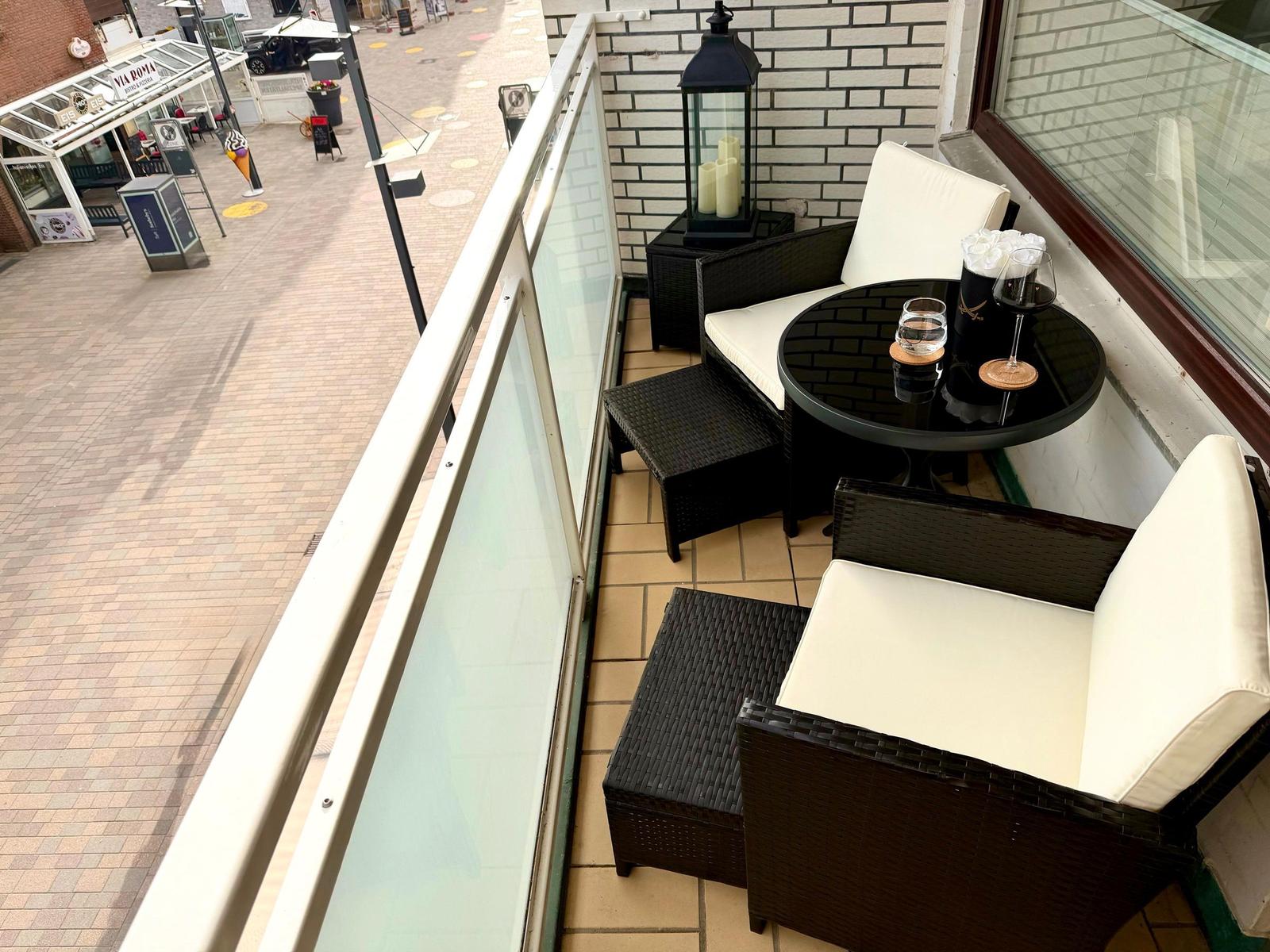 Terrasse mit zwei Stühlen, Tisch und Laterne. Blick auf belebte Straße.