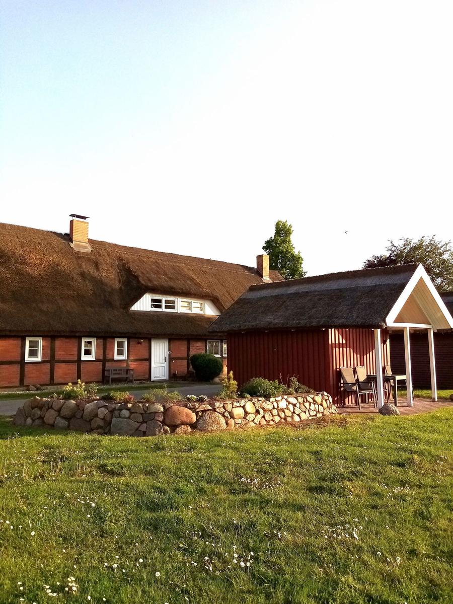 Rotes Holzhaus mit Strohdach und Gartenbereich mit Tisch und Stühlen.