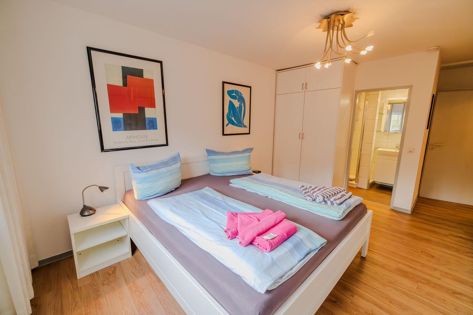 Schlafzimmer mit Doppelbett, Kleiderschrank und Blick in das Badezimmer.