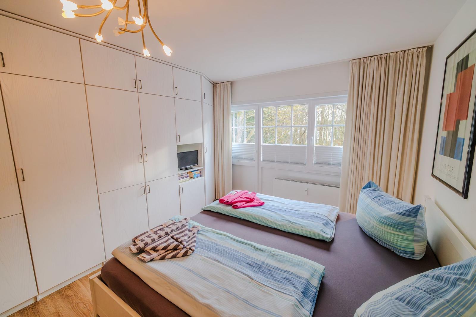 Schlafzimmer mit Doppelbett, weißen Schränken und Fenster mit Blick auf Bäume.