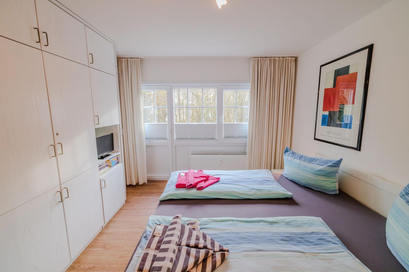 Schlafzimmer mit zwei Betten, großem Schrank und Fenster mit Blick auf Bäume.