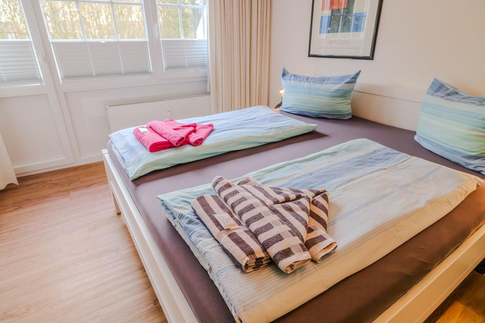 Ein Bett mit Bettwäsche und Handtüchern. Fenster, Wandbild und Holzboden.